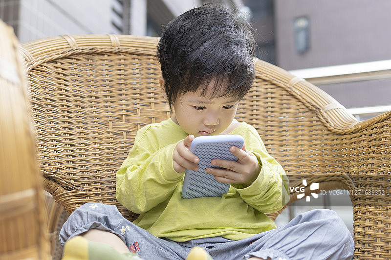 中国小女孩在阳台的藤椅上玩手机图片素材