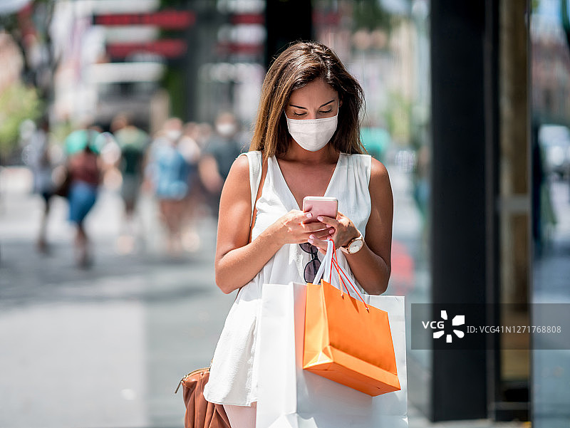 在街上购物和发短信时戴着口罩的美丽女人图片素材