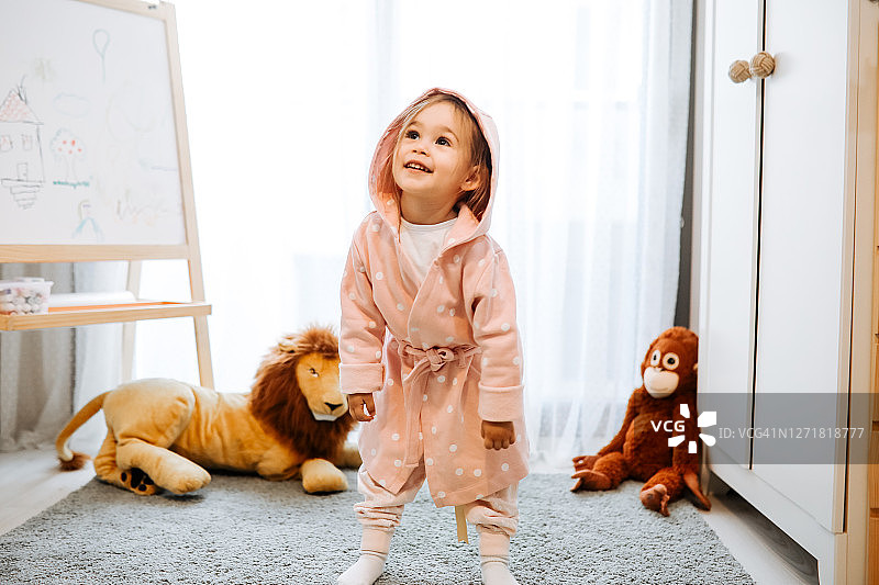 在阳光明媚的卧室里喂玩具娃娃的可爱小女孩图片素材