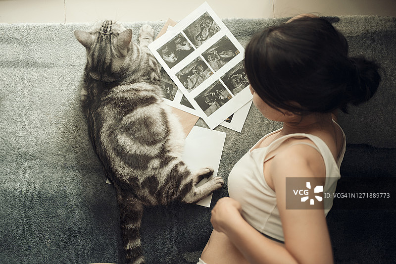快乐的亚洲孕妇看着超声波图片，查看宝宝的情况，可爱的猫咪陪伴图片素材
