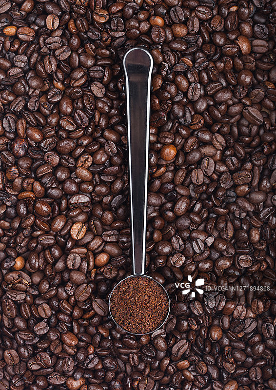 咖啡豆上的银色钢勺中的新鲜有机咖啡粉。图片素材