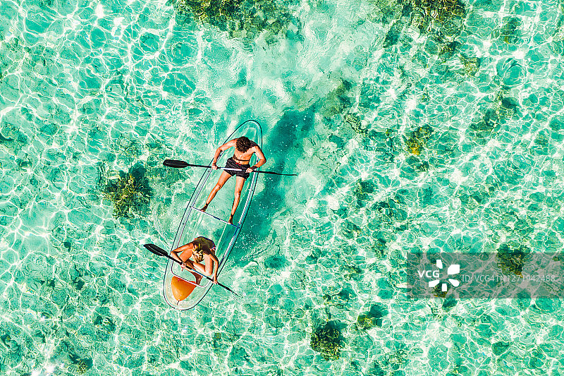 年轻夫妇在热带海洋中划着玻璃底皮划艇图片素材