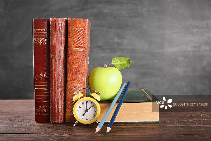 书堆、苹果、时钟和彩色铅笔在黑色黑板背景的木桌上。留白图片素材