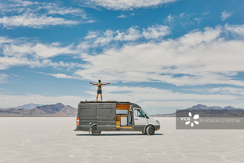 年轻男人站在露营车顶在博纳维尔盐滩图片素材