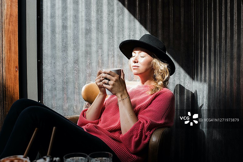 女人坐在咖啡馆里喝着热饮享受阳光图片素材