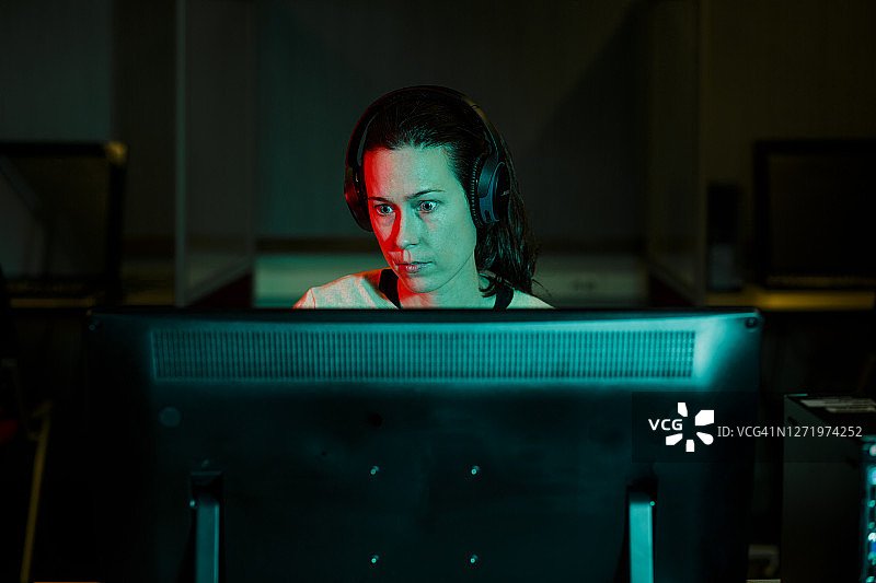 女子目光专注地在黑暗房间里操作台式电脑图片素材
