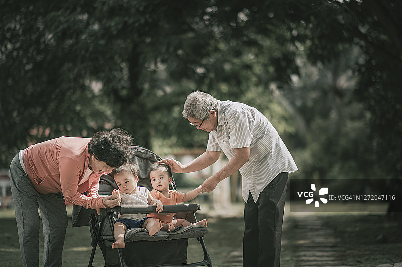 亚裔祖父母在早晨的公园里与他们的双胞胎男婴孙子互动图片素材