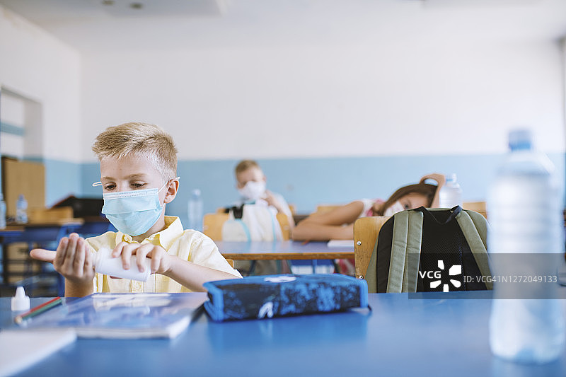 在教室里用免洗洗手液的戴口罩男学生图片素材