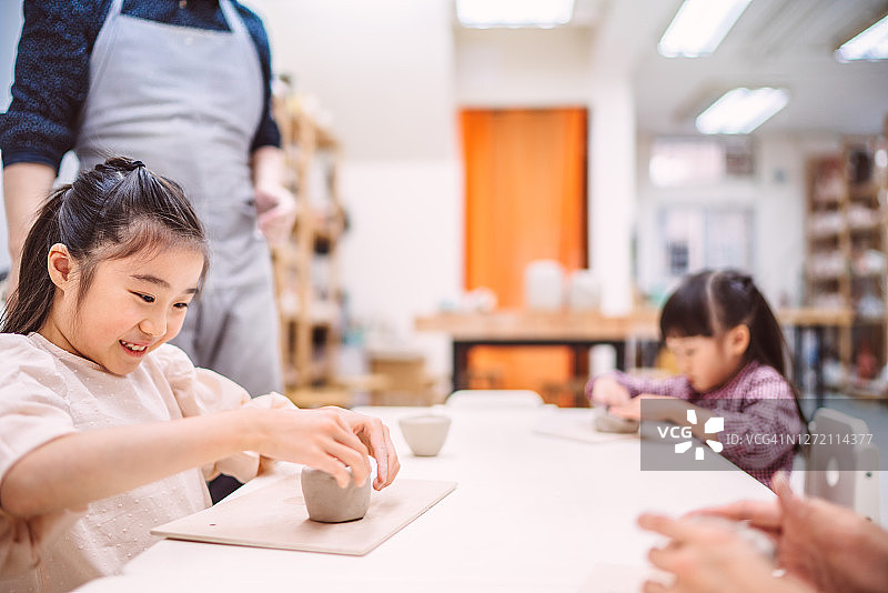 可爱的小女孩在陶艺师的指导下用粘土制作陶杯图片素材