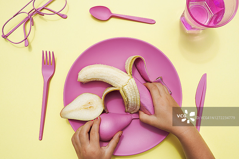 女婴的手从塑料盘中拿起粉红色的梨和香蕉图片素材