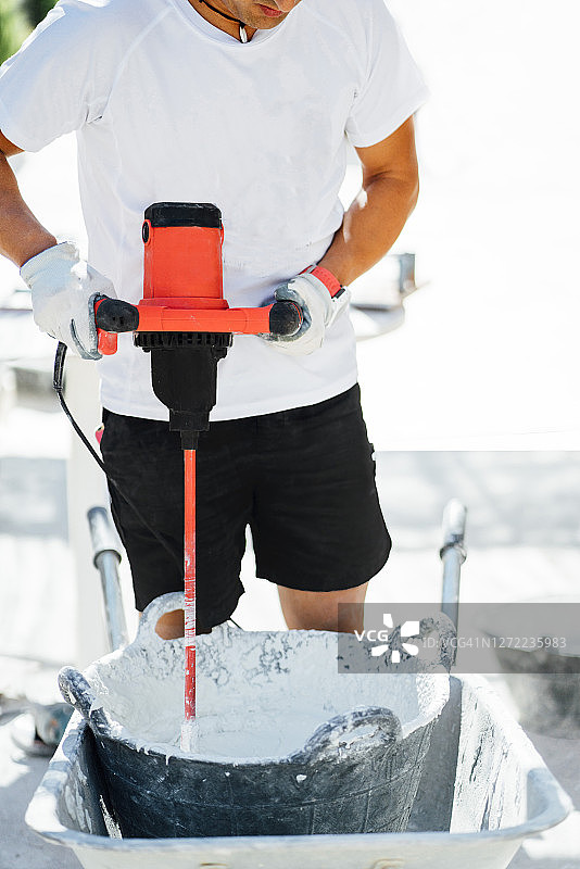 男人在建筑工地用机器在桶里搅拌水泥图片素材