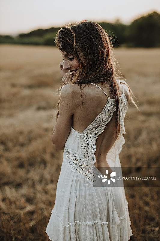 身穿白色连衣裙站在麦田里回头的女人图片素材