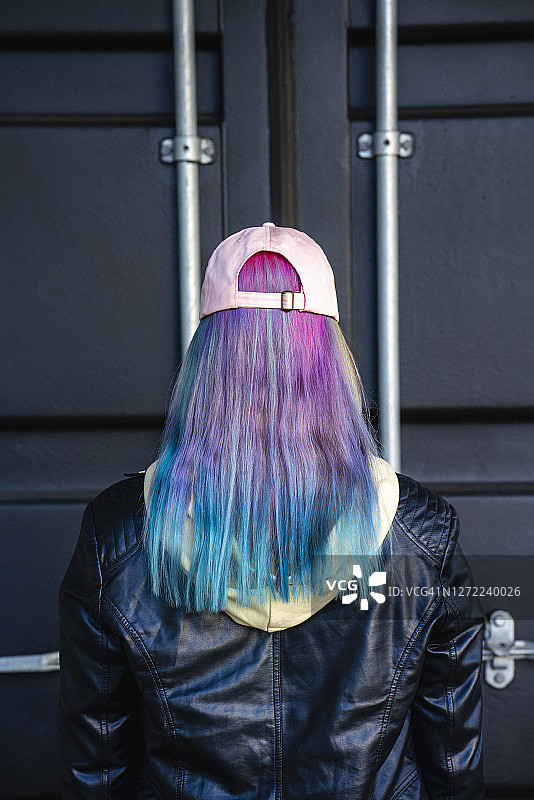 染发的年轻女子站在黑色集装箱前的背影图片素材