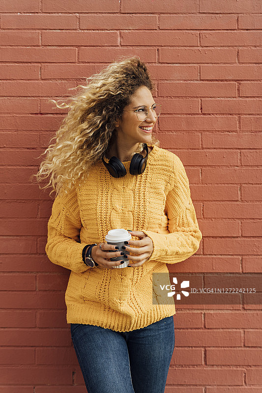 年轻漂亮的金色头发女子拿着一次性咖啡杯靠在红色砖墙上图片素材