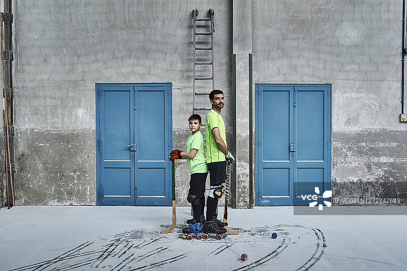 父子在球场门口背靠背拿着曲棍球杆图片素材