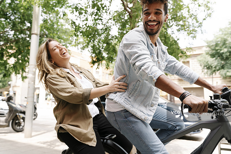 快乐的年轻夫妇在城市里享受电动自行车之旅图片素材