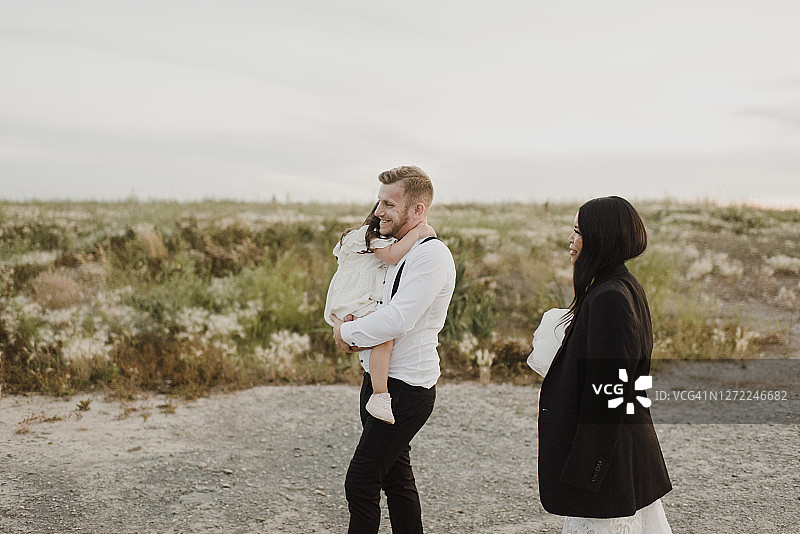 微笑的父亲抱着女儿，母亲在田野里行走图片素材