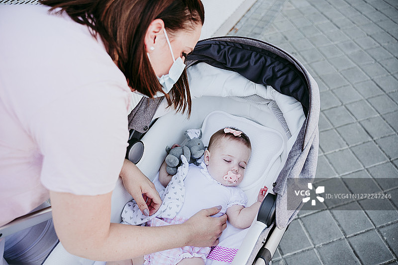 母亲戴着防护口罩，婴儿在婴儿车里睡觉图片素材