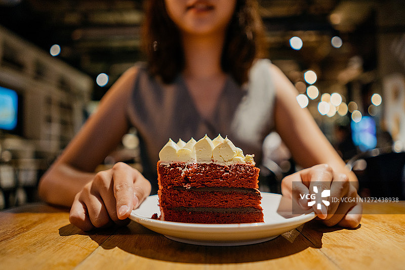 年轻亚裔女子在咖啡馆享用红丝绒蛋糕图片素材