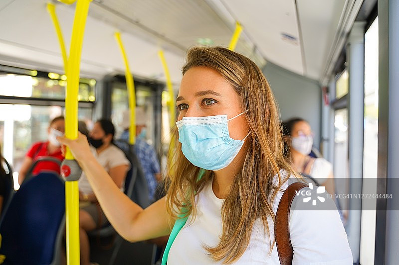 年轻女人在公共汽车上保持社交距离并戴着外科口罩图片素材