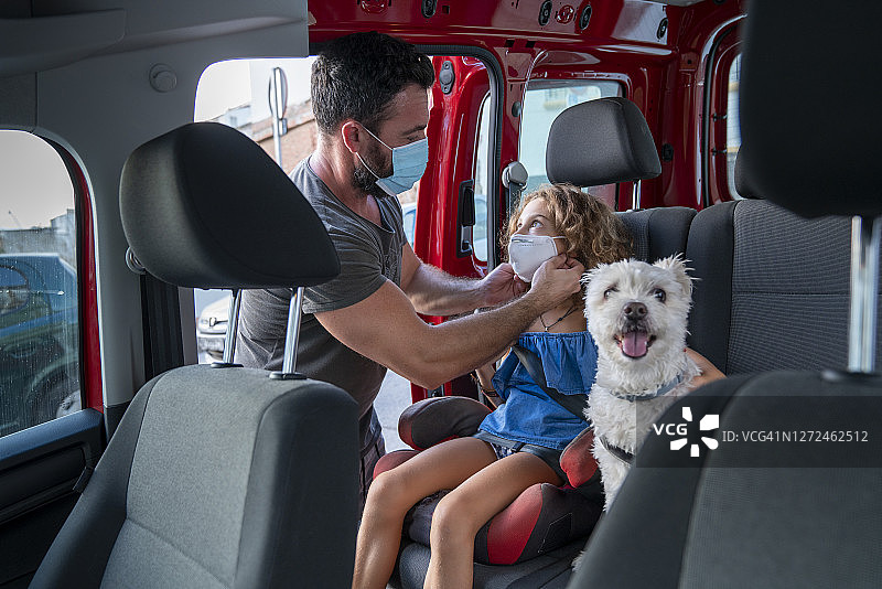 父亲帮助女儿在汽车座椅上戴口罩图片素材