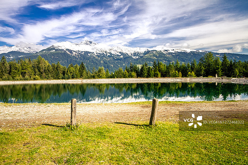 奥地利利恩茨的清澈山湖，蓝天背景下的云彩、绿色云杉和雪山图片素材