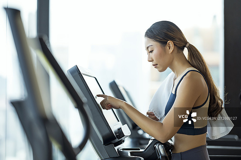 有魅力的年轻女子在健身房跑步机上选择锻炼计划的侧视图图片素材