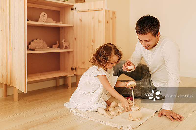 父亲在舒适的家中与小女儿在游戏室里玩玩具，父亲节图片素材