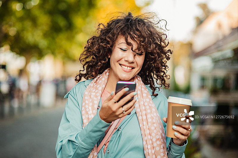 穿着蓝色外套的女人在街上微笑并拿着智能手机图片素材