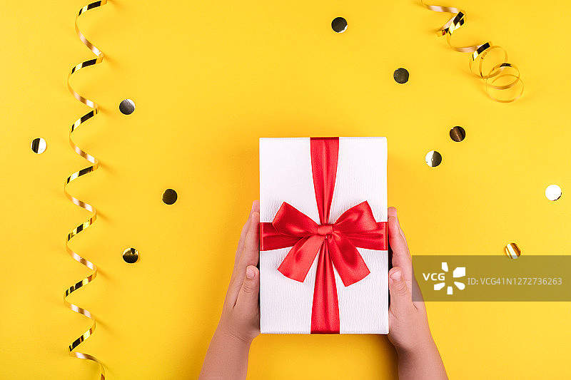 孩子的手在黄色背景上拿着礼品盒图片素材