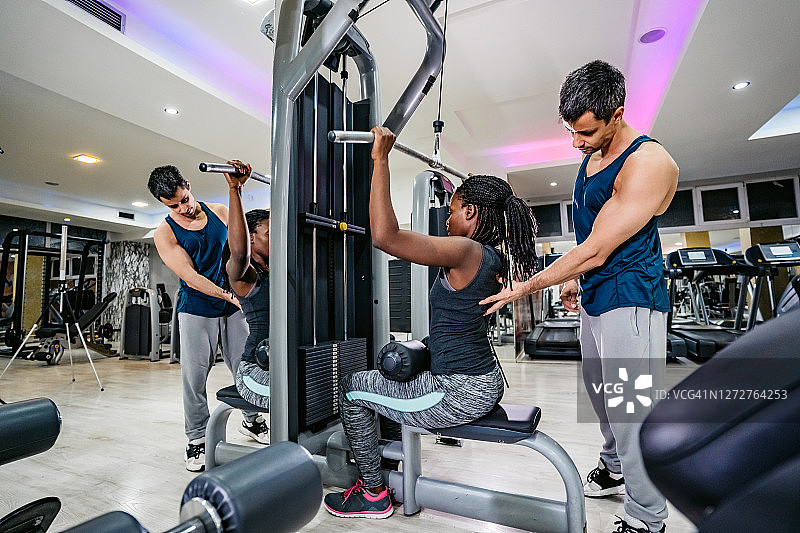 健身教练帮助女士在健身房锻炼图片素材