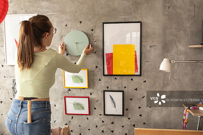 年轻女人在装饰客厅时将手表挂在墙上图片素材