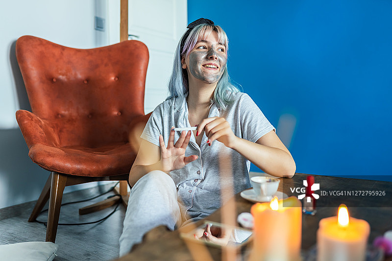 微笑的女人在客厅里涂指甲油并看向别处图片素材