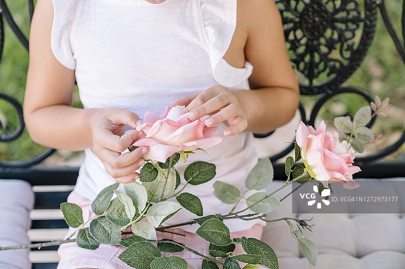 坐在花园里看手中玫瑰的匿名6岁女孩图片素材