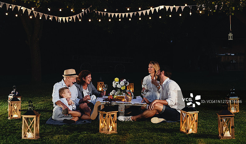 多代同堂家庭在夏日花园派对上，夜晚坐在草地上图片素材