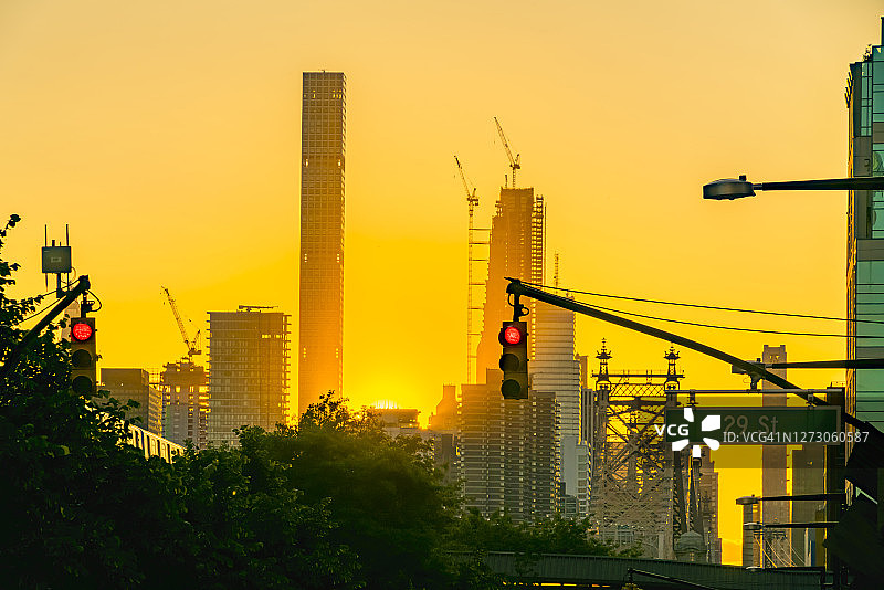 纽约地铁在长岛市皇后广场高楼间的绿叶树木之上的高架铁轨上运行图片素材