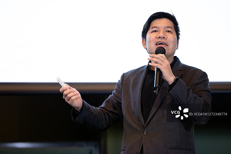 亚洲男讲师在投影仪屏幕前使用麦克风和激光笔图片素材