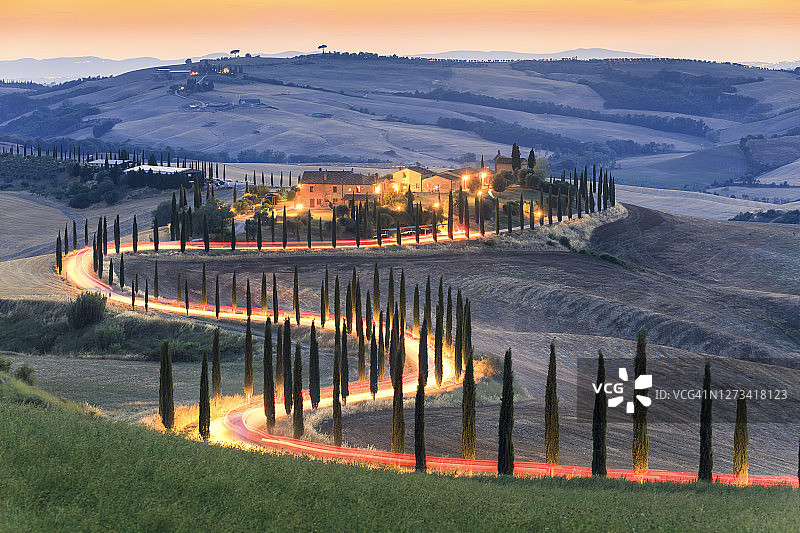 瓦尔多尔恰，锡耶纳，托斯卡纳。日落时农舍柏树路上的车灯图片素材