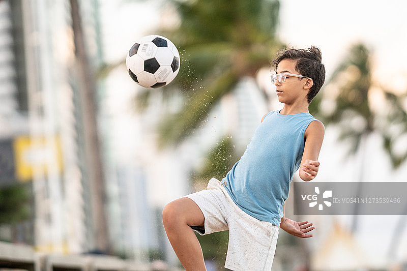 男孩在海滩上踢足球图片素材