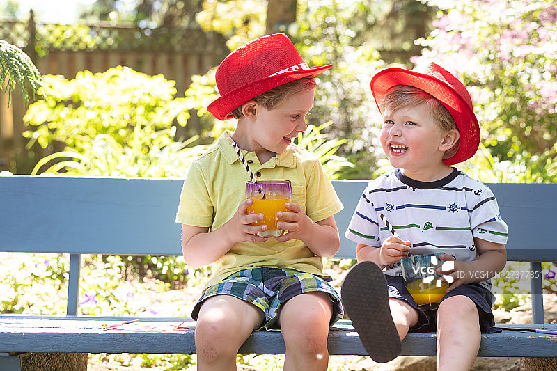 坐在户外长椅上用吸管喝饮料的兄弟俩图片素材
