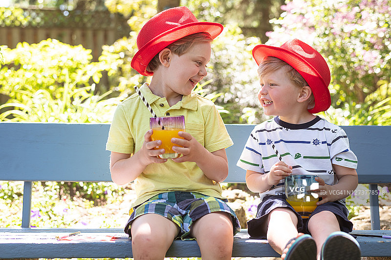 坐在户外长椅上用吸管喝饮料的兄弟俩图片素材