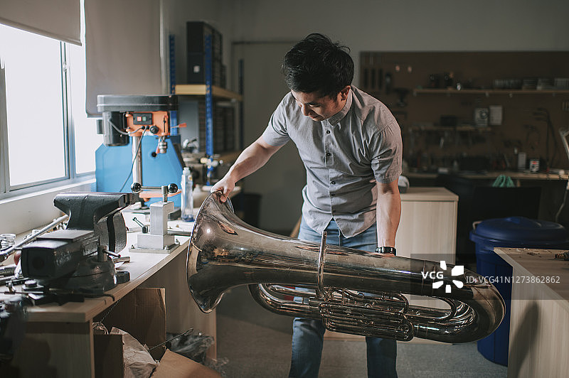 华人男子在工作室检查维修小号图片素材