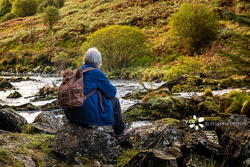 坐在苏格兰西南部乡村河流岩石旁的老年男人图片素材