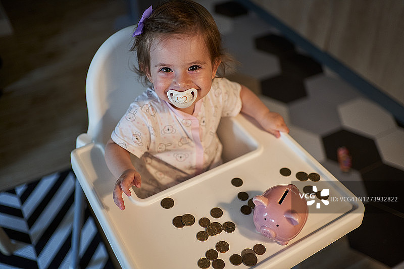 高脚椅上欣喜的婴儿与存钱罐图片素材