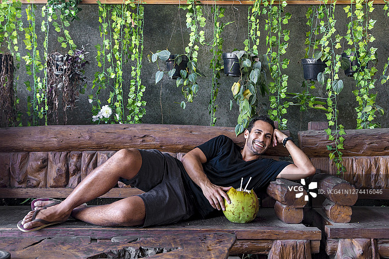 快乐的游客躺在长椅上喝椰子汁，印度尼西亚巴厘岛图片素材