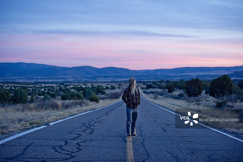 男子站在日落时孤独的沙漠公路上，吉拉荒野，美国新墨西哥州图片素材