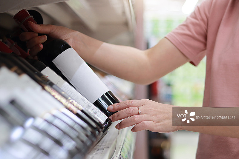 女人从超市货架上拿酒精饮料。在商店购买酒精图片素材