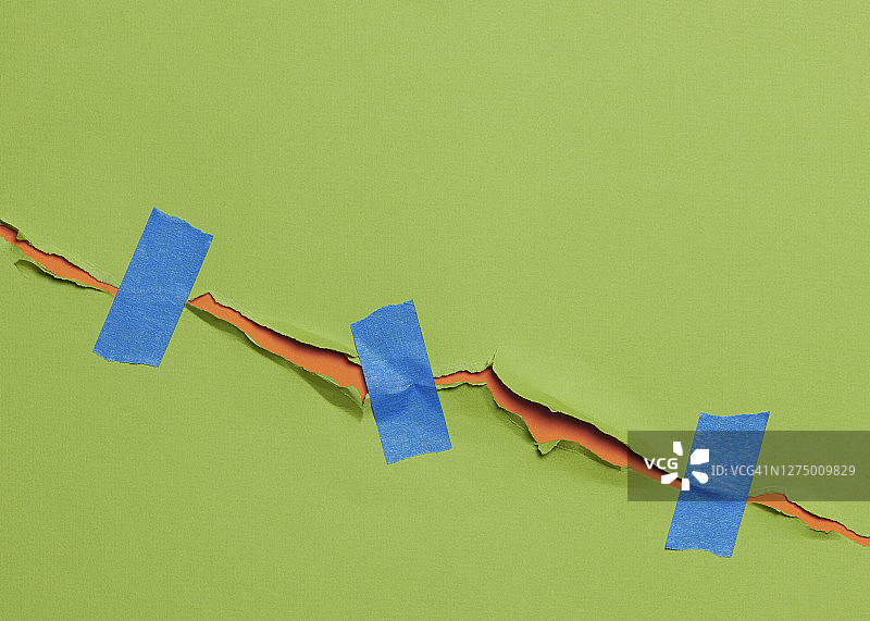 撕裂的绿色纸张（用蓝色胶带粘在一起），露出下面的橙色纸张图片素材