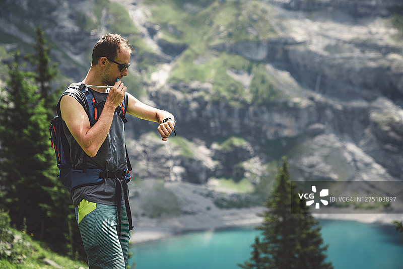 男人在厄希嫩湖徒步旅行时，用管子喝水并看运动手表图片素材