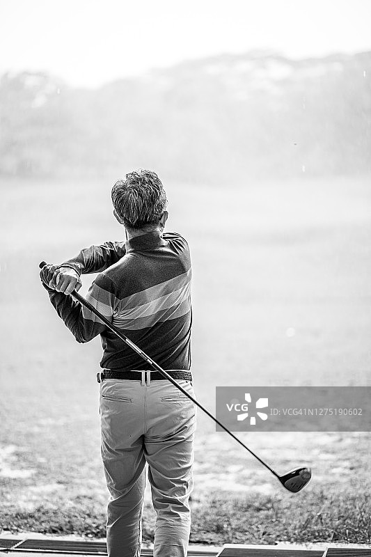 在雨天高尔夫球练习场挥杆的亚洲高尔夫球手图片素材